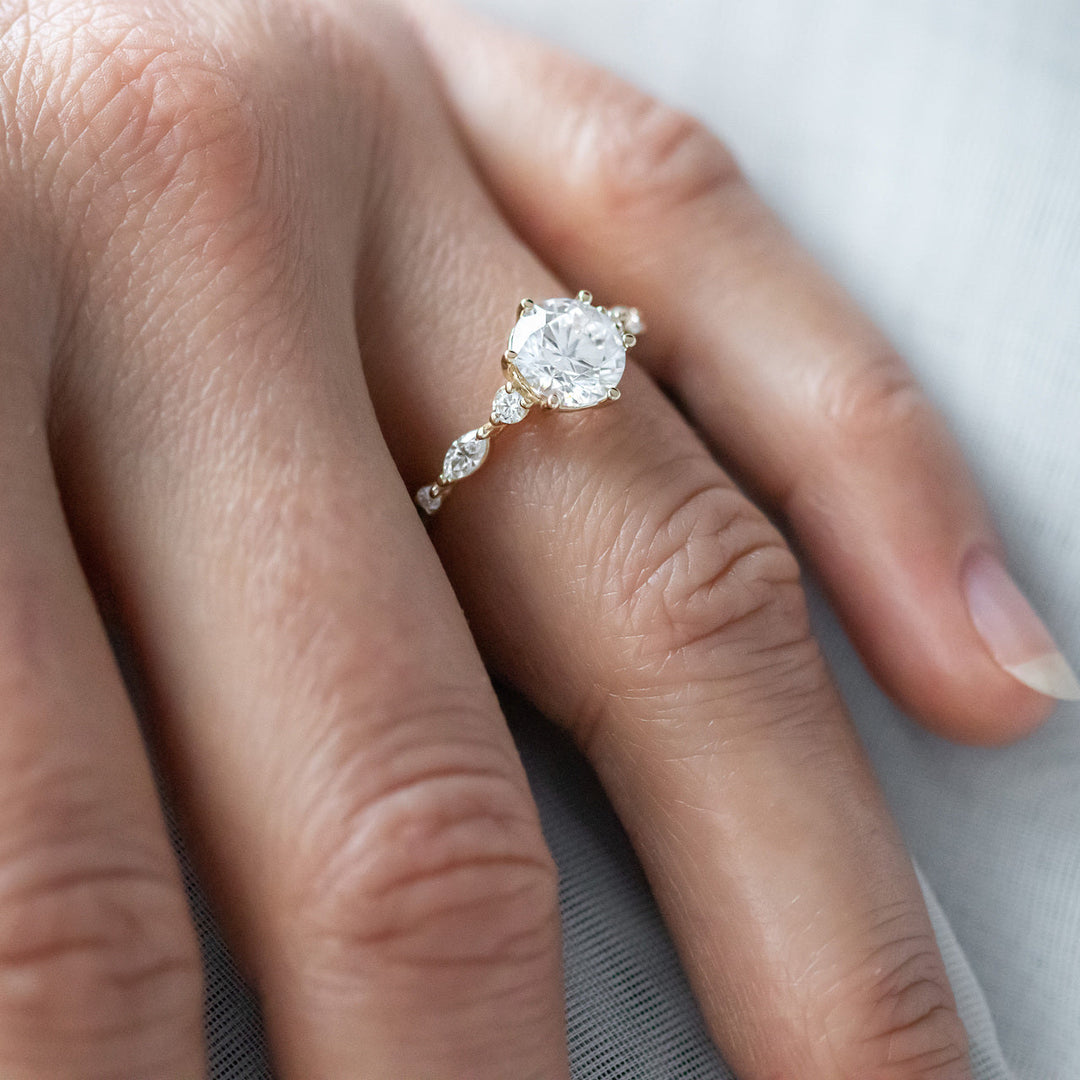 A person's hand displaying a round cut pave moissanite diamond engagement ring with gold band.
